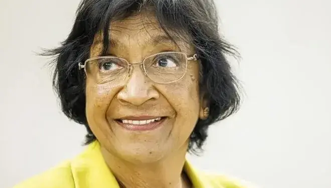 Retrato de mujer profesional sonriente con gafas y blazer amarillo, mirando hacia arriba. Representa liderazgo y visión.