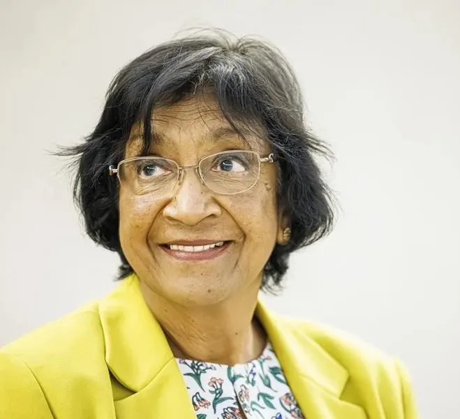 Retrato de mujer profesional sonriente con gafas y blazer amarillo, mirando hacia arriba. Representa liderazgo y visión.