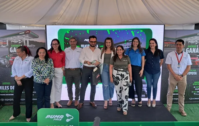 Grupo de nueve personas posando sonrientes en un escenario frente a una pantalla con la marca Puma Pris.
