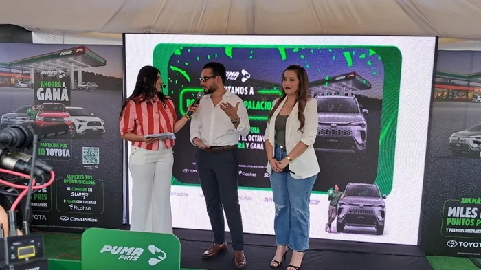 Tres personas en un evento corporativo frente a una pantalla LED gigante con anuncios comerciales.