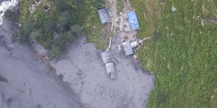 Vista aérea de un paisaje afectado por lodo o un deslizamiento, con estructuras rurales junto a un río y vegetación verde.