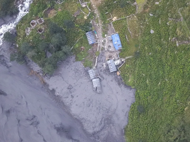 Vista aérea de un paisaje afectado por lodo o un deslizamiento, con estructuras rurales junto a un río y vegetación verde.