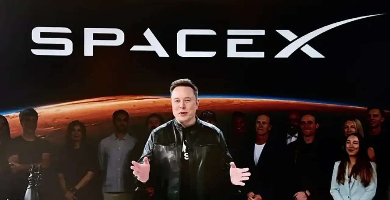 Elon Musk hablando frente a un fondo con el logotipo de SpaceX y una imagen de la Tierra.
