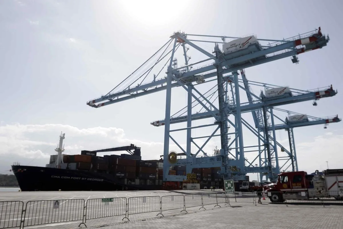 Grúas pórtico gigantes y un barco portacontenedores cargado en una terminal portuaria bajo un cielo despejado.