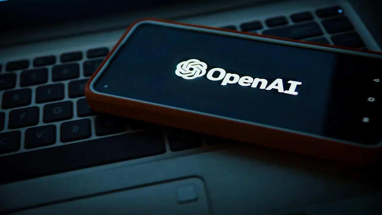 Smartphone con estuche naranja mostrando el logotipo brillante de OpenAI sobre un teclado de computadora portátil.