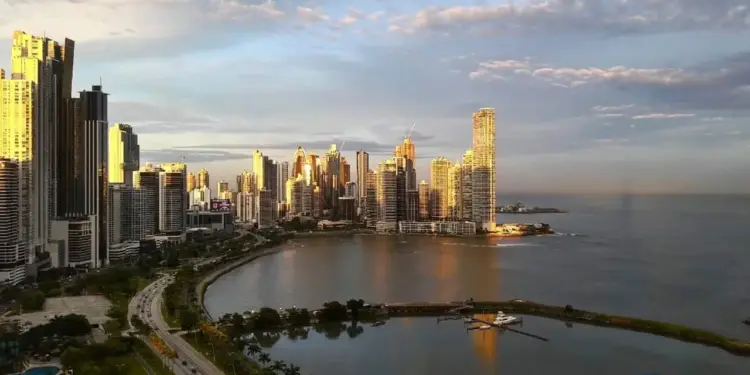 Vista panorámica del horizonte de una ciudad moderna con rascacielos junto a la costa y una bahía al atardecer.