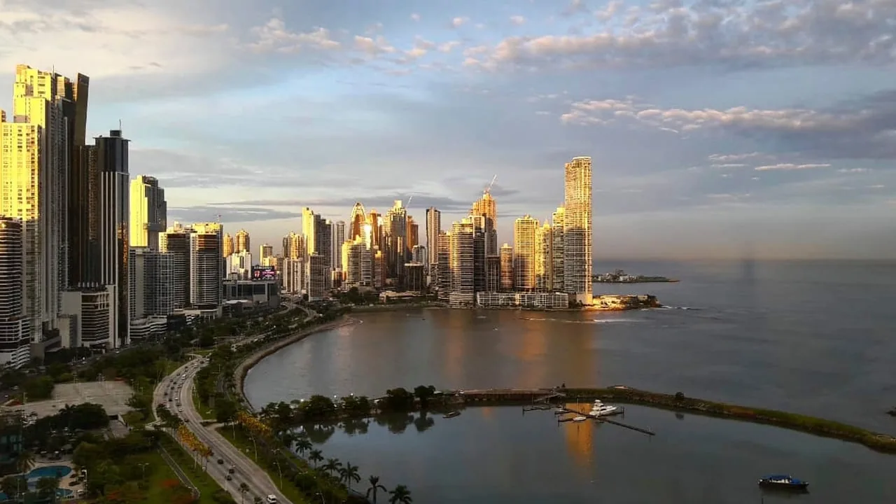 Vista panorámica del horizonte de una ciudad moderna con rascacielos junto a la costa y una bahía al atardecer.