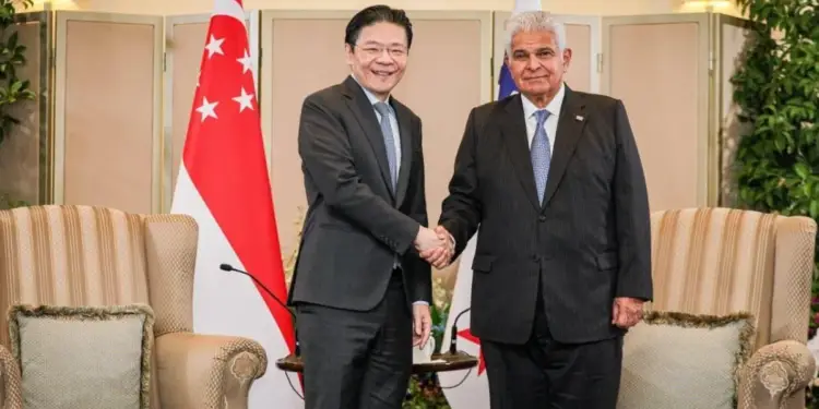 Dos hombres de negocios, uno asiático y otro de ascendencia del Medio Oriente, se dan la mano frente a las banderas de Singapur e Israel en un entorno formal.