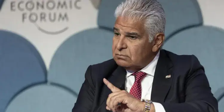 Un hombre de negocios con traje y corbata roja gesticula frente al panel del World Economic Forum.