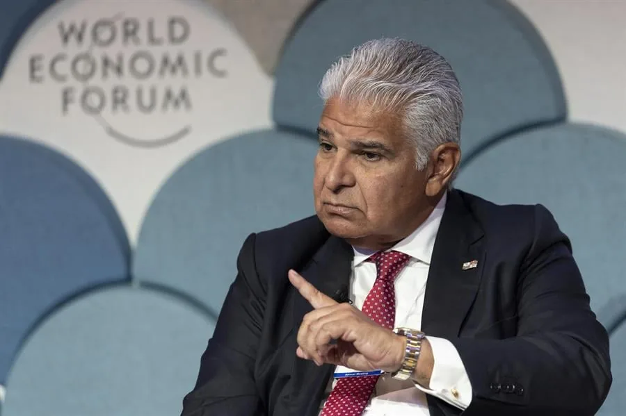 Un hombre de negocios con traje y corbata roja gesticula frente al panel del World Economic Forum.