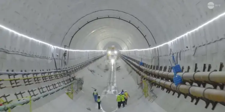 Grupo de trabajadores con chalecos de seguridad en el interior de un gran túnel en construcción con tuberías.