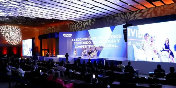 Panelistas discuten sobre la economía de los medios, contenido, tecnología y competitividad global en un evento empresarial con una gran pantalla de fondo.