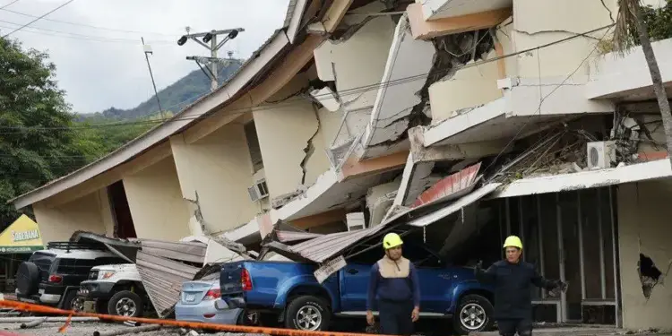 Vista de un edificio con daños estructurales severos y colapso parcial, con vehículos sepultados y personal de emergencia.