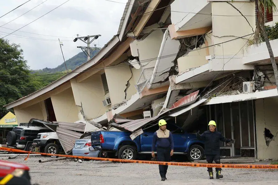 Vista de un edificio con daños estructurales severos y colapso parcial, con vehículos sepultados y personal de emergencia.