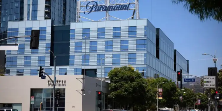 Vista exterior de un edificio moderno de oficinas con el logotipo de Paramount en la azotea y tráfico vehicular en la calle.