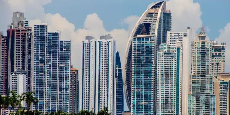 Horizonte urbano con rascacielos modernos y edificios altos. Un edificio con diseño curvo resalta. Vegetación en primer plano bajo cielo azul.