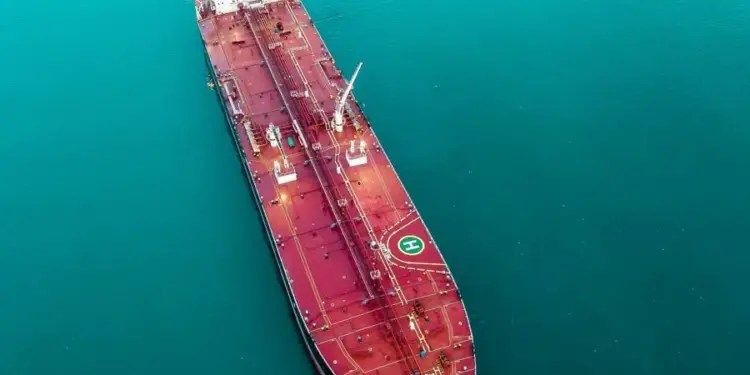 Vista aérea de un gran superpetrolero de color rojo oscuro navegando en aguas turquesas, mostrando su cubierta con tuberías y una helisuperficie.
