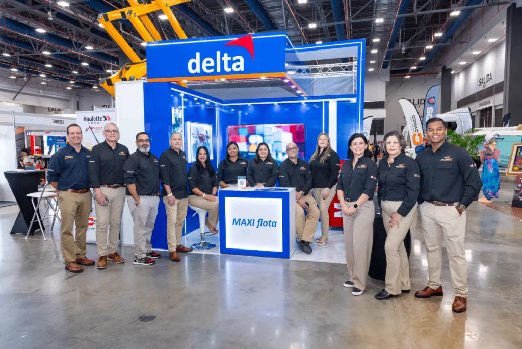 Grupo de profesionales en camisas negras y pantalones caqui posando frente a un stand azul y blanco en una feria comercial.