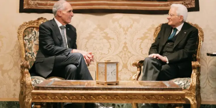 Dos hombres con traje formal sentados en sillones clásicos durante una reunión profesional.
