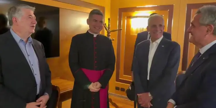 Cuatro hombres, uno vestido de clérigo y tres con trajes de negocios, sonríen y conversan en un entorno profesional interior.
