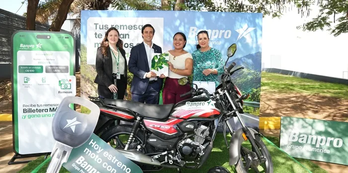 Cuatro personas posan junto a una motocicleta nueva frente a un cartel corporativo con una pantalla publicitaria.