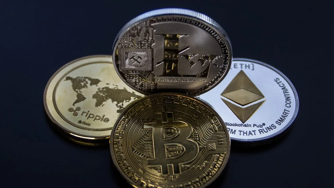 Primer plano de varias criptomonedas físicas: Bitcoin, Ethereum, Ripple y Litecoin, dispuestas sobre una superficie oscura. Representan activos digitales y el futuro financiero.