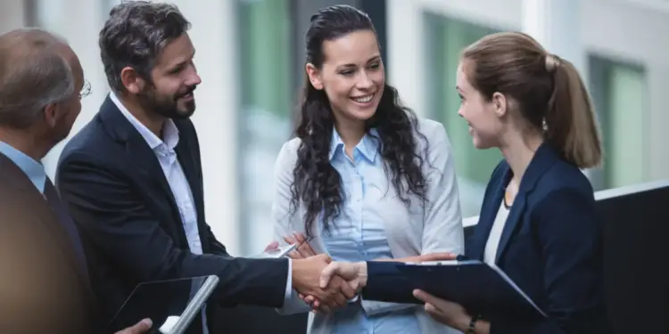 Cuatro profesionales de negocios reunidos en una oficina corporativa estrechando las manos mientras sonríen.