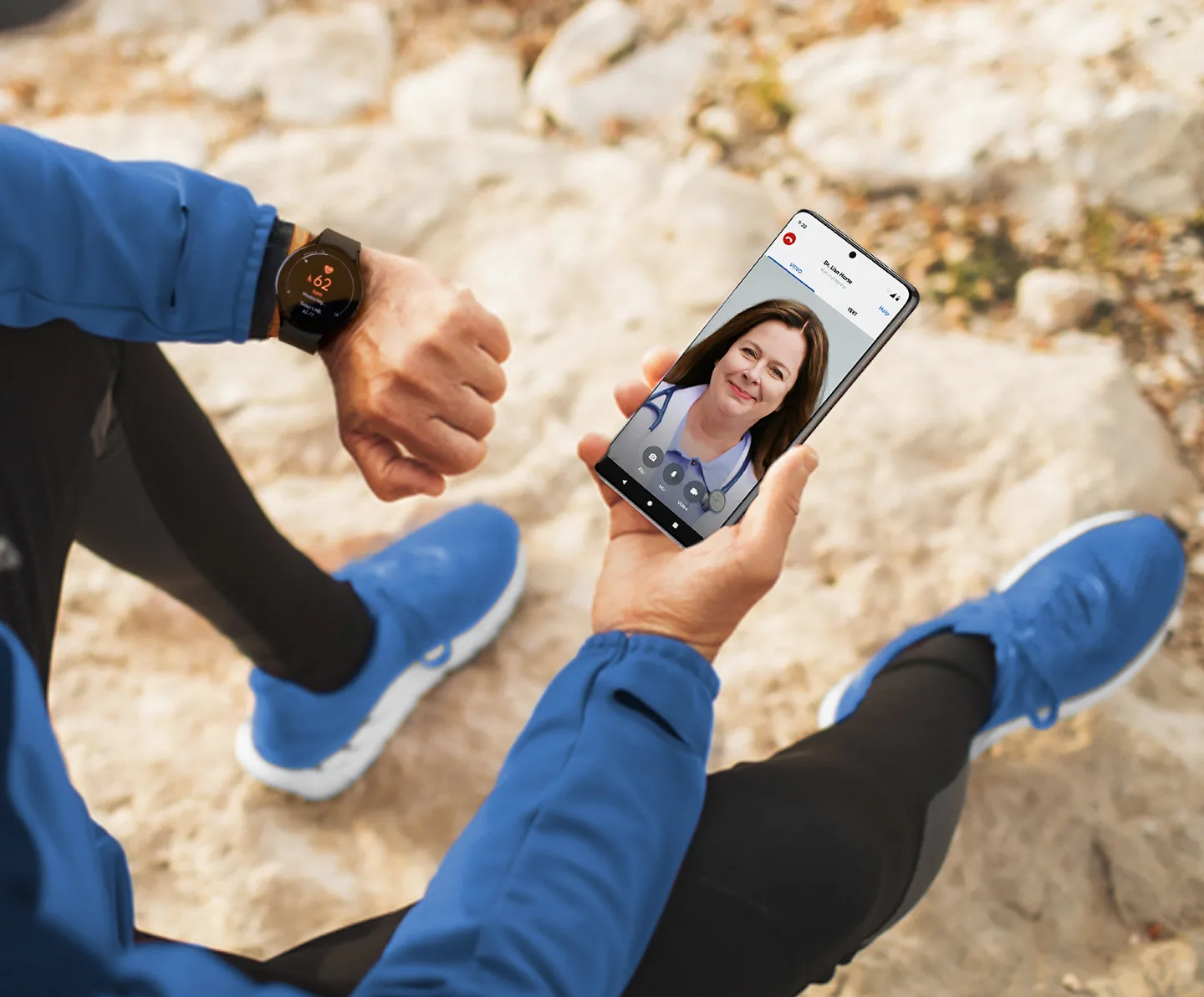 Persona sentada en rocas usando un reloj inteligente y realizando una videollamada médica en el teléfono móvil.