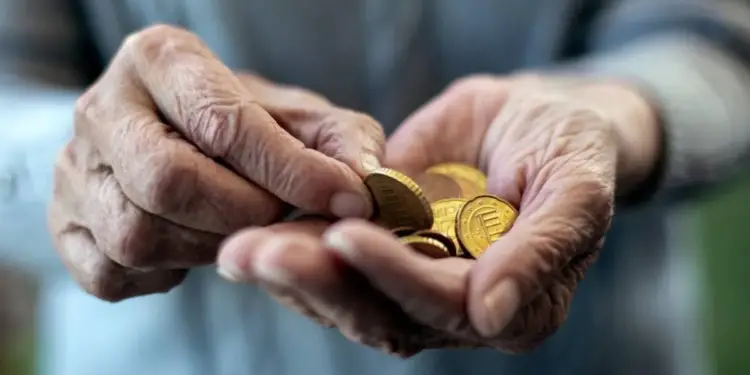 Primer plano de las manos arrugadas de una persona mayor contando varias monedas de euro en la palma de su mano.