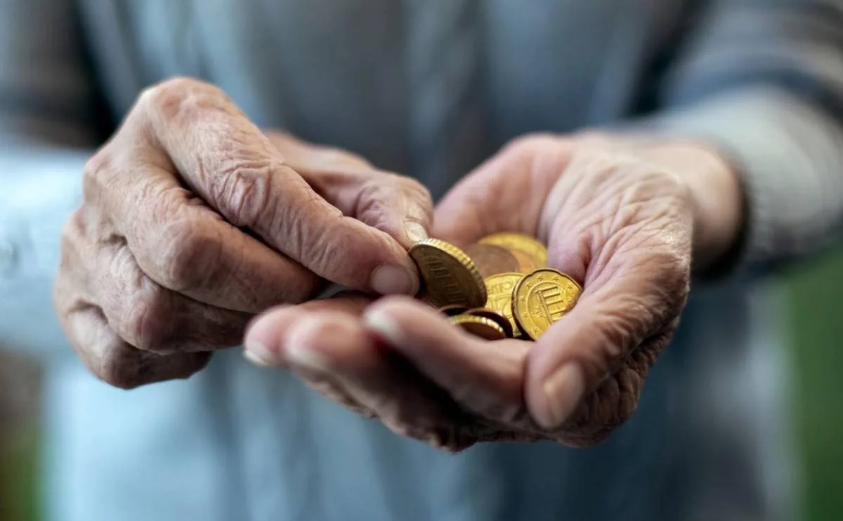 Primer plano de las manos arrugadas de una persona mayor contando varias monedas de euro en la palma de su mano.