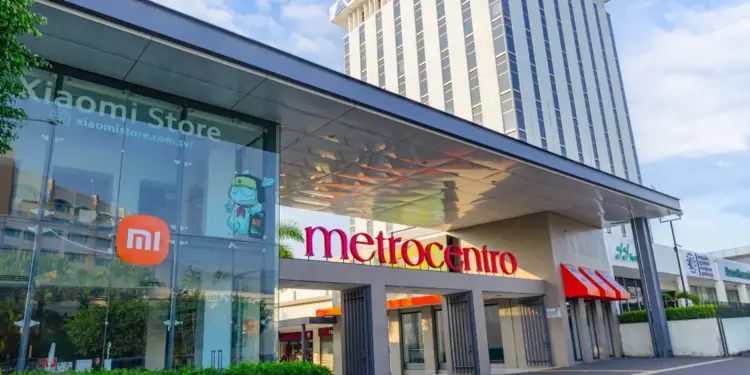 Fachada de un complejo comercial con la tienda Xiaomi, el letrero "metrocentro" y un edificio corporativo alto. Se observan logos de CEPA y Banco Promerica.
