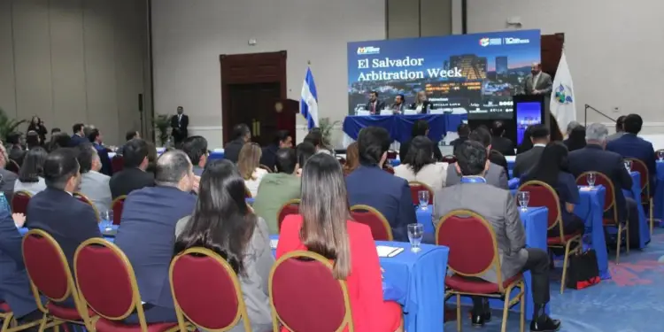 Audiencia en un evento de negocios y arbitraje en El Salvador, con ponentes en un escenario y bandera nacional.