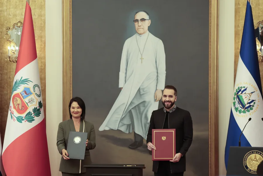 Dos autoridades muestran documentos firmados frente a las banderas de Perú y El Salvador.