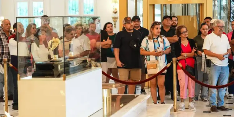 Grupo diverso de personas observando una vitrina con un objeto de exhibición en un amplio salón interior.