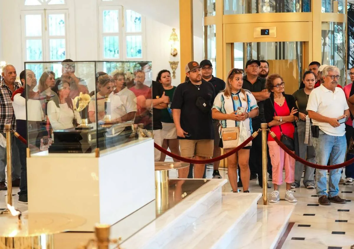 Grupo diverso de personas observando una vitrina con un objeto de exhibición en un amplio salón interior.