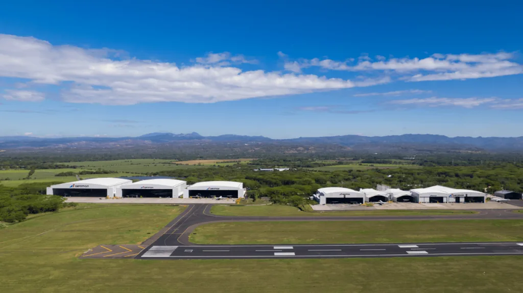 Vista aérea de varios hangares industriales y pistas de aterrizaje rodeados de vegetación y montañas al fondo.