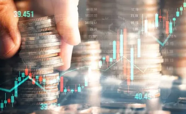 Mano apilando monedas sobre un fondo de gráficos financieros con velas alcistas y bajistas, y una línea de tendencia. Representa inversión y crecimiento económico.