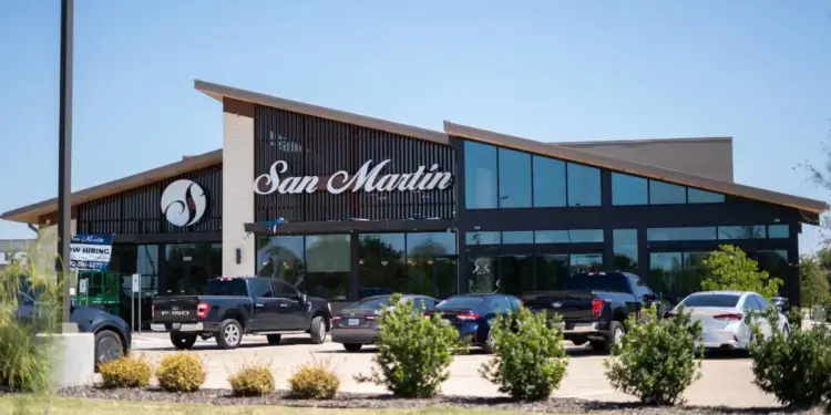 Fachada de un edificio comercial moderno con el letrero San Martin y vehículos estacionados frente al local.