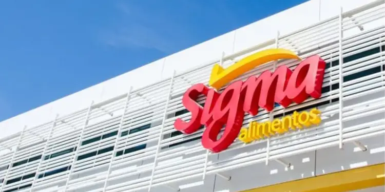Fachada de un edificio moderno con el logotipo rojo y amarillo de Sigma Alimentos en letras tridimensionales, bajo un cielo azul claro.