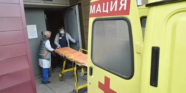 Personal médico con mascarilla sacando una camilla desde una ambulancia amarilla hacia un edificio.