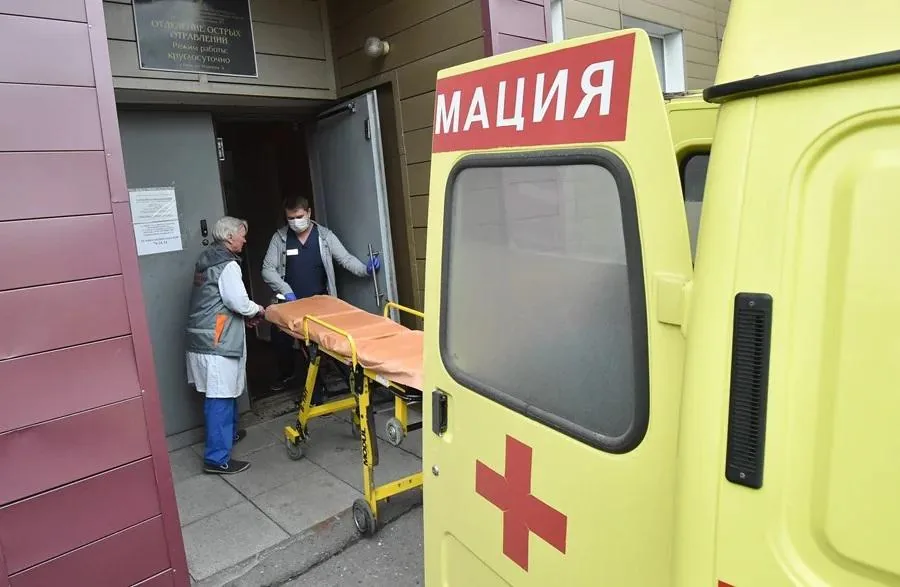 Personal médico con mascarilla sacando una camilla desde una ambulancia amarilla hacia un edificio.