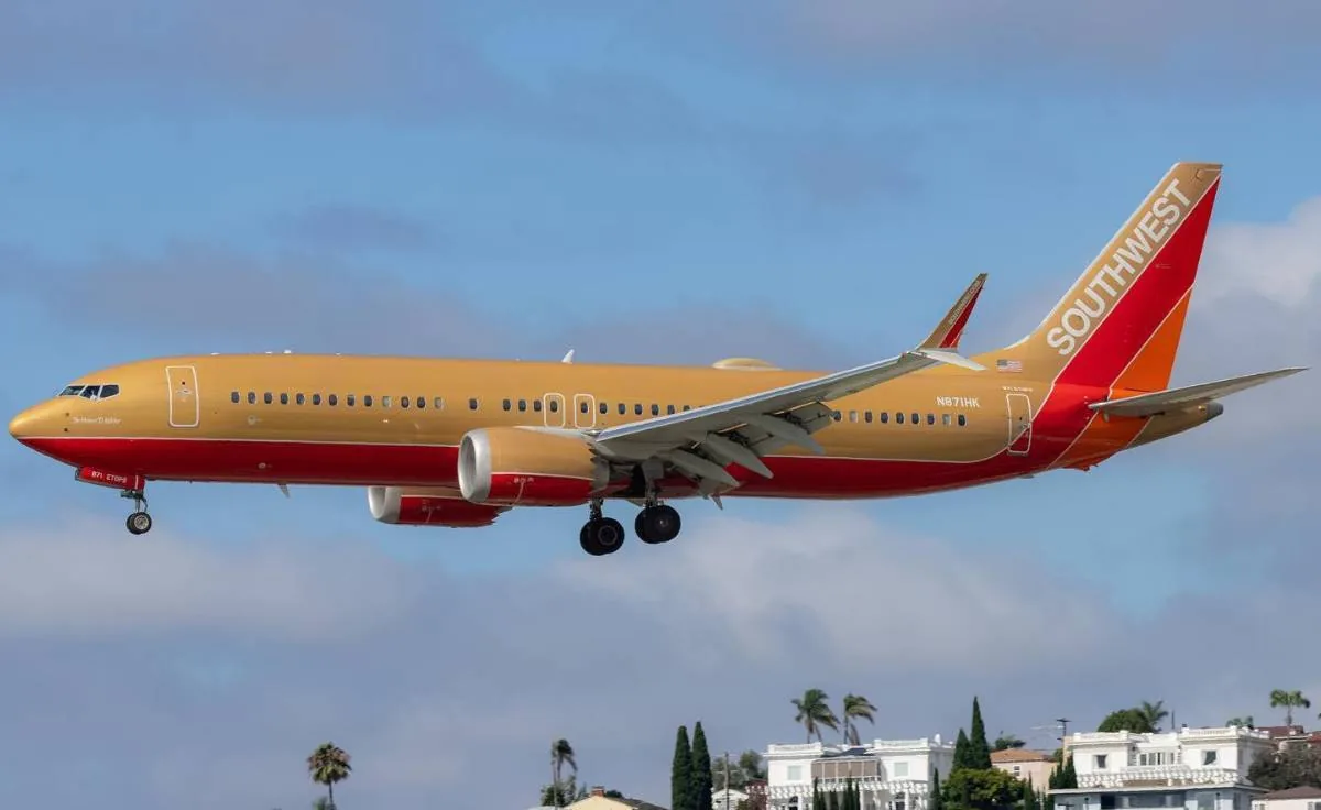 Avión comercial de Southwest Airlines con fuselaje dorado y franjas rojas y naranjas en la cola, aterrizando o despegando con el tren de aterrizaje desplegado.