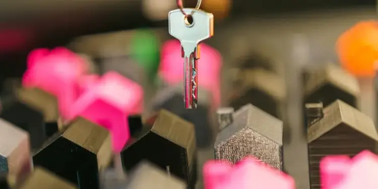 Primer plano de una mano sosteniendo un llavero con una llave plateada, sobre un fondo de miniaturas de casas de diversos colores, simbolizando la inversión inmobiliaria.