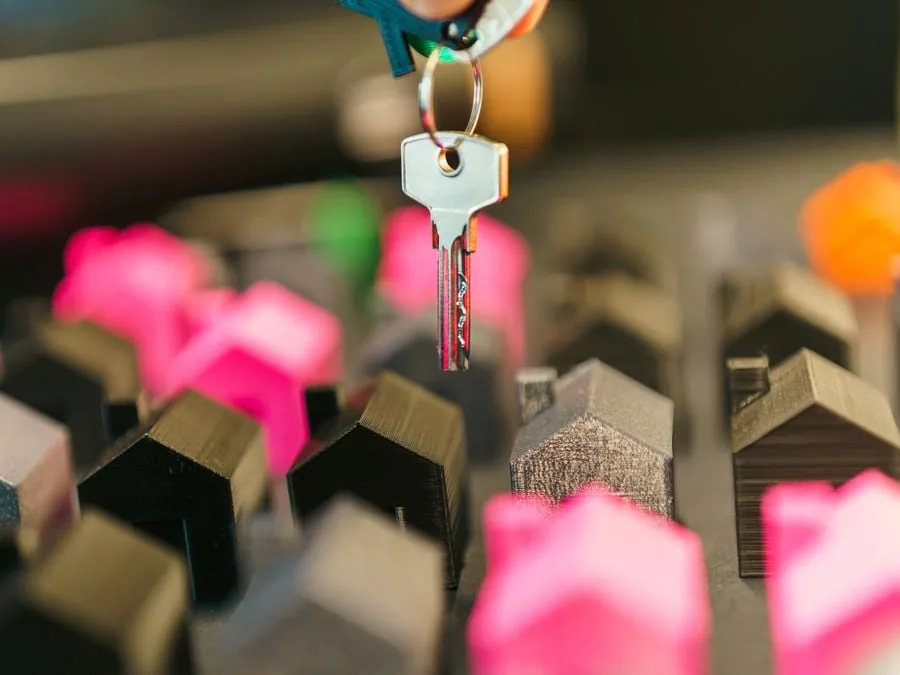Primer plano de una mano sosteniendo un llavero con una llave plateada, sobre un fondo de miniaturas de casas de diversos colores, simbolizando la inversión inmobiliaria.