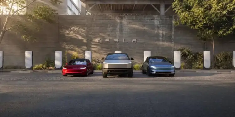 Tres vehículos eléctricos estacionados frente a una pared de concreto con el logotipo de Tesla y múltiples estaciones de carga.