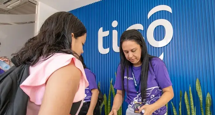 Empleada de atención al cliente atendiendo a una persona en una recepción con pared azul de listones.
