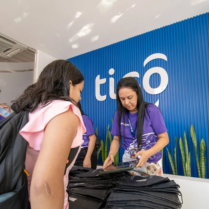 Empleada de atención al cliente atendiendo a una persona en una recepción con pared azul de listones.