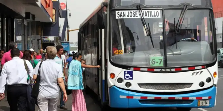 Autobús urbano detenido en la calle mientras personas caminan por la acera y una mujer aborda el vehículo.