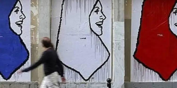 Mural urbano con tres rostros femeninos de perfil usando velos azul, blanco y rojo. Un peatón pasa rápidamente por delante.