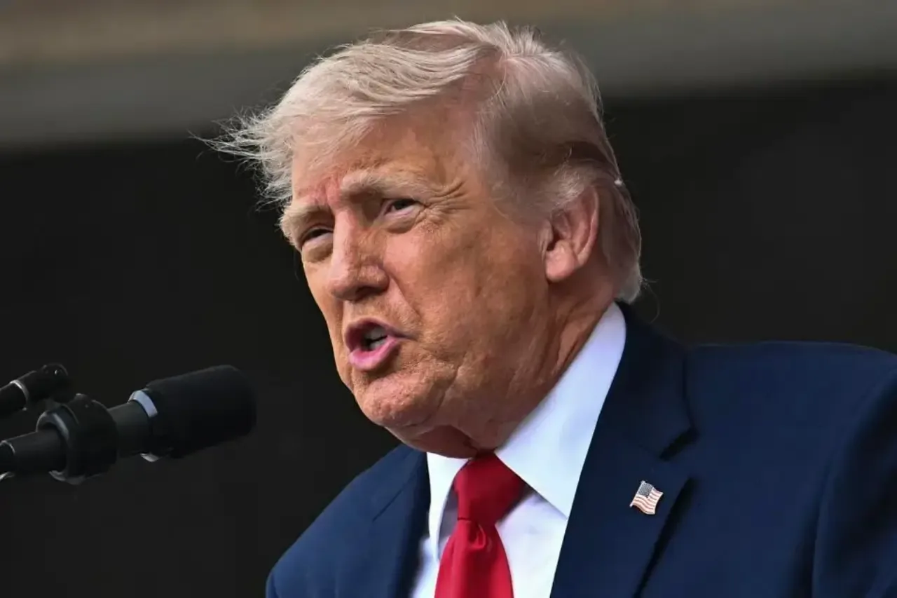Retrato de medio cuerpo de Donald Trump hablando ante un micrófono con traje azul y corbata roja.